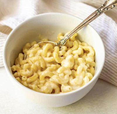 White bowl filled with macaroni and cheese that has a serving spoon in it.